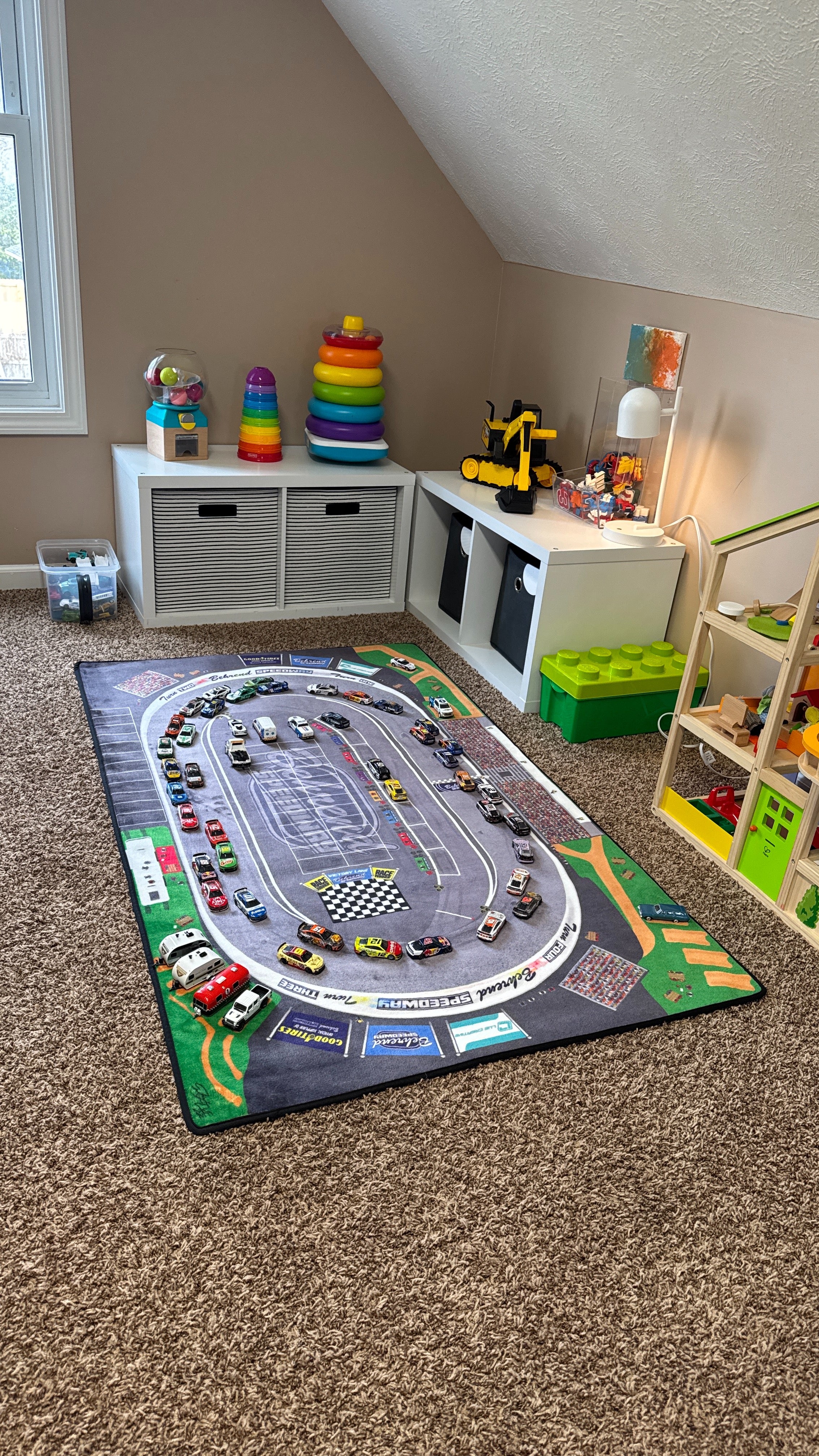 Children's playroom with a large race track rug, toys, and storage units.