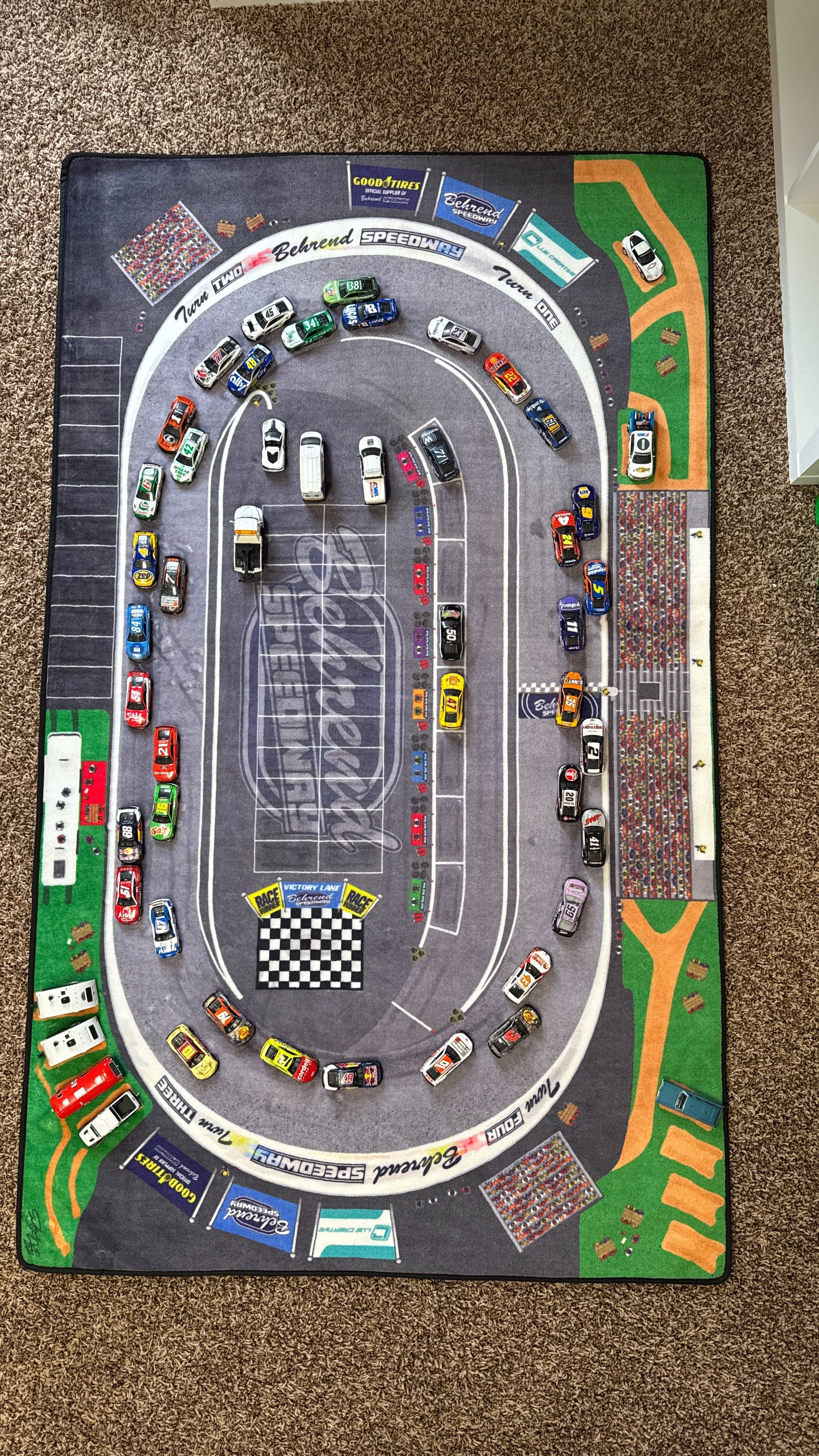 Car racing track mat with toy cars on a carpeted floor