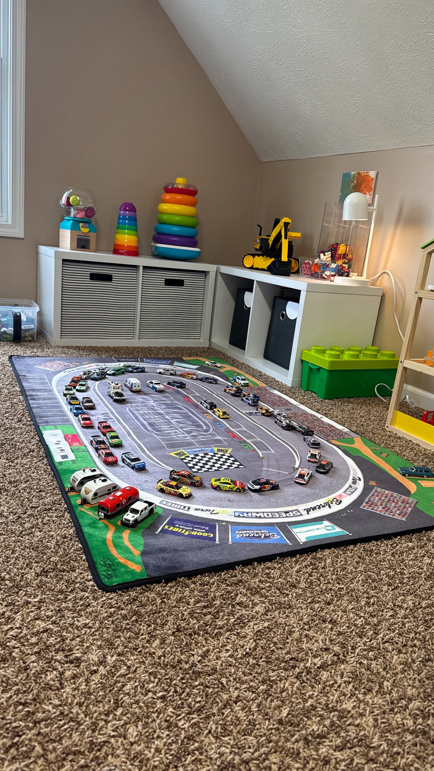 Children's playroom with a race track rug, toys, and storage units.