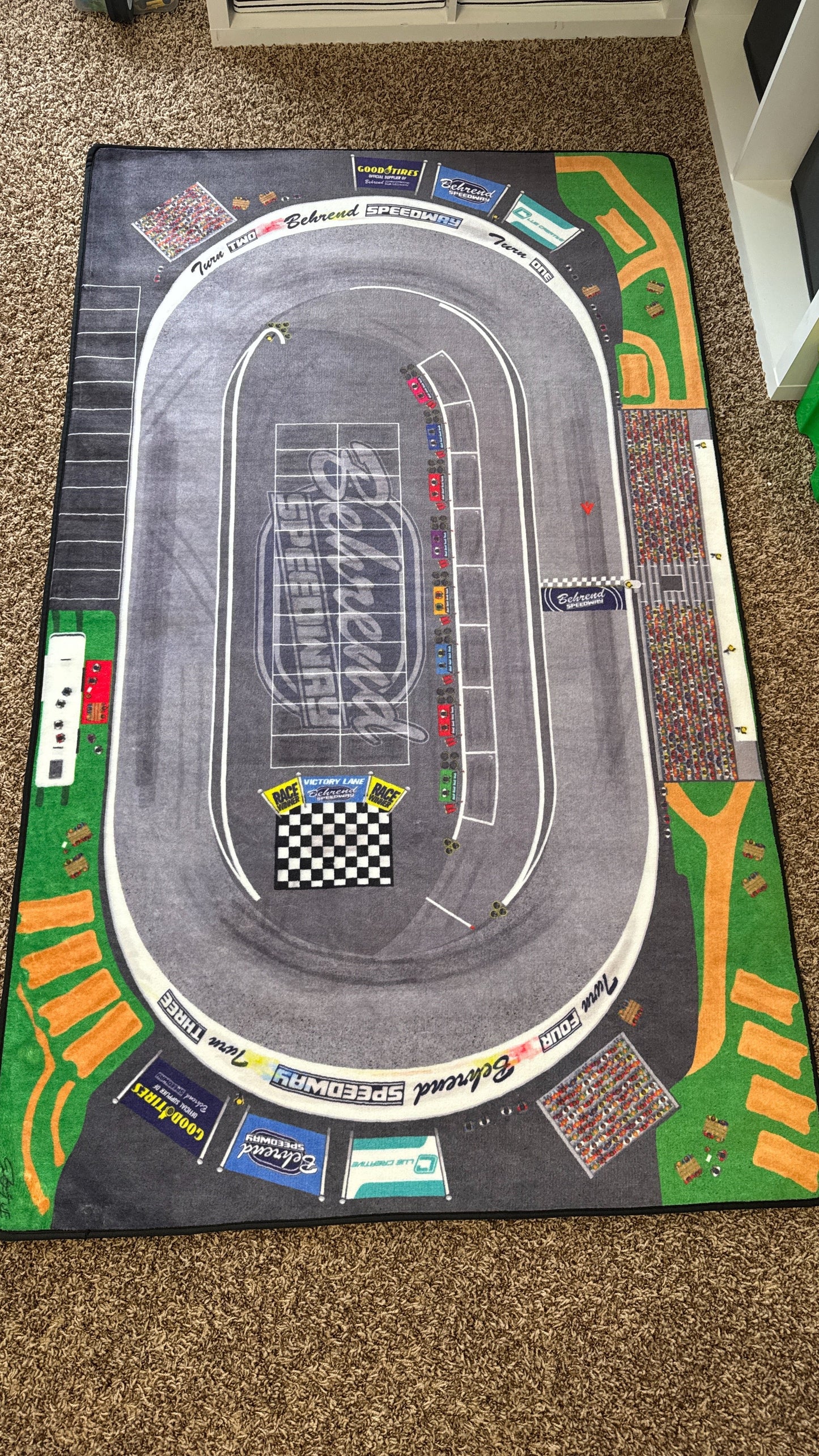 Racing track mat with car illustrations on a carpeted floor